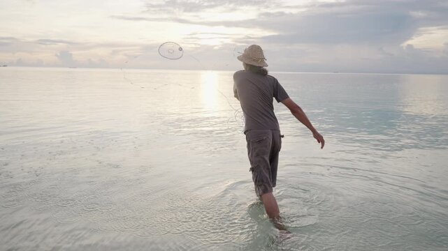 An asian fisherman casting or throwing a fishing net in the sea in indonesia, southeast asia, wearing a hat, slow motion shot