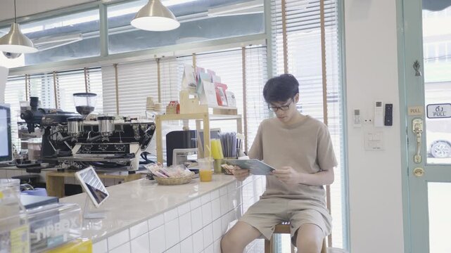 A serene scene in a showcasing a young individual immersed in reading a digital device while enjoying a drink. Natural light filters through large windows, creating a welcoming atmosphere for relaxati