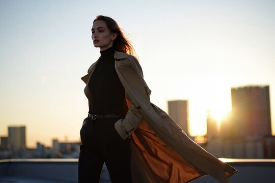 Woman Holding Long Coat at Urban Rooftop During Sunset with City Skyline