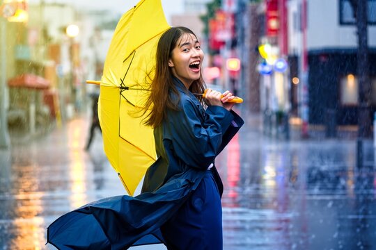 Woman Laughing Under Yellow Umbrella in Rainy Urban Night Street