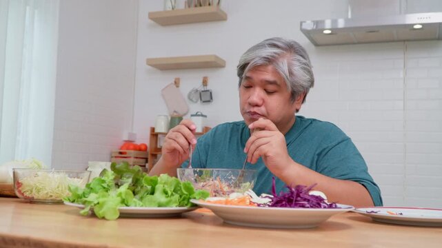 Asian elderly man preparing salad in kitchen, representing healthy food, wellness, nutrition, and lifestyle concept in cheerful indoor environment with vegetables, positive atmosphere
