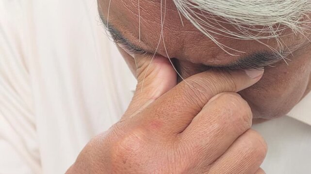 South East Asian old senior man rubbing his dry eye due to the overusing of screen time, getting eye fatigue or optical problem, closeup shot