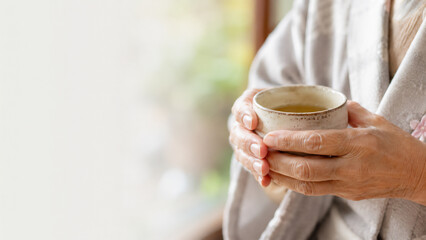 Close up of gentle elderly hands holding a warm cup with no face visible, respect for the aged day care and gratitude banner with copy space