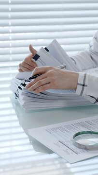 Person examining business documents on a desk with a magnifying glass, analyzing financial reports for an audit, tax, or accounting process