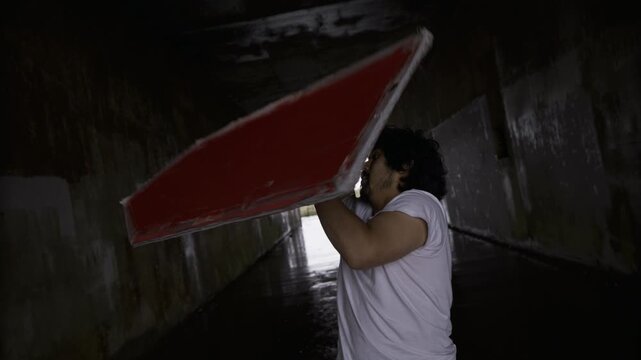 Silhouette Of Man Spinning Large Red Sign Overhead Inside Concrete Tunnel - Steady Cam Medium Shot