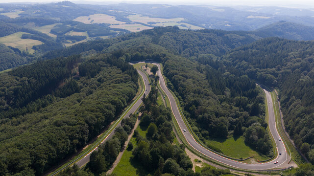 Herschbroich, Rheinland-Pfalz, Germany - 23 June 2026: Aerial view of the Caracciola-Karussell at the Nurburgring race track, surrounded by dense green forests and rolling hills.