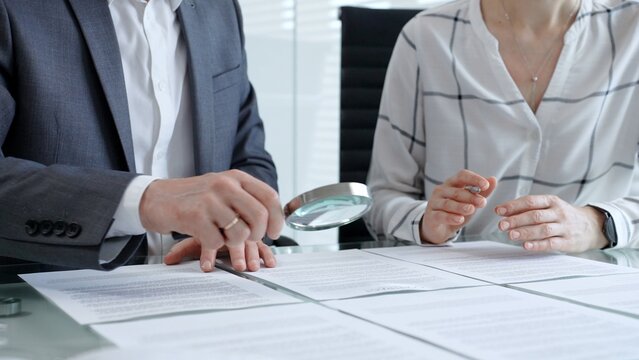 Business professionals reviewing legal contracts and important documents with a magnifying glass, performing careful examination and due diligence for risk assessment