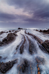 Fototapeta premium Stunning long exposure landscape of the famous flysch rock formations on the beach of Barrika under a moody blue sky during twilight in northern Spain