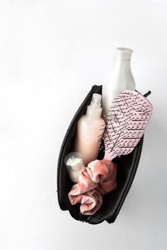 Black travel pouch filled with essential hair products: pink paddle brush, two cosmetic bottles (shampoo, spray), small jar, velvet scrunchie, ready for travel or gym.