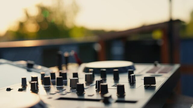 adjusting controls on a wooden surface of a mixer in an outdoor environment with trees and sunlight. dynamic and focused perspective on a dj's hand and mixer controls.