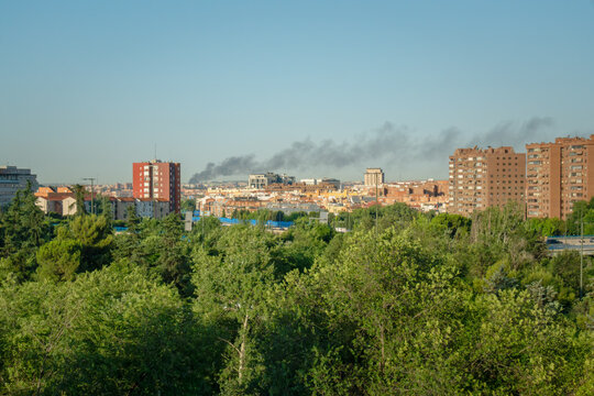 Smoke plumes rising over madrid residential buildings and green trees highlighting environmental issues
