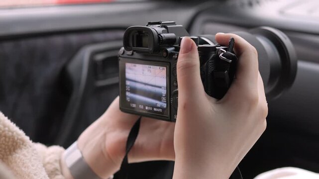 Hands hold camera inside car, preparing to shoot. Focused fingers adjust settings on screen. Person ready to capture road trip moments. Ideal for travel, vlog, or automotive content