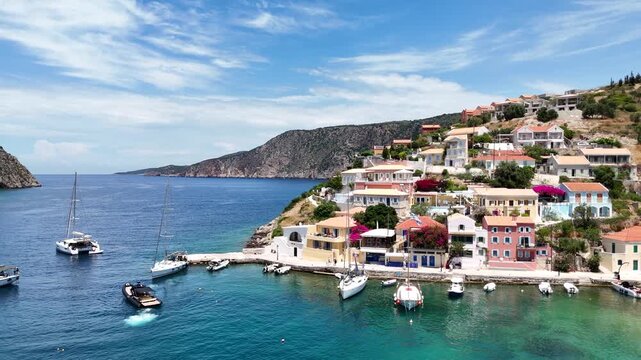 Aerial drone video of Assos village in Kefalonia, Greece, with colorful waterfront buildings, anchored boats, turquoise waters, and scenic Mediterranean coastal views