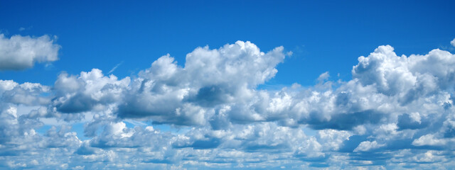 Panoramic view of white cumulus clouds against bright blue sky. Wide nature banner with large copy space. Concept of good weather, atmosphere and natural background. © Dmitrii Labrador