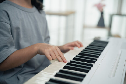 Child practicing piano with focused hands pressing keys on white keyboard in bright indoor environment learning music instrument