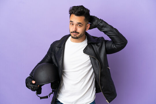Young man with a motorcycle helmet isolated on purple background having doubts