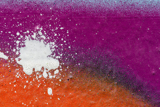 Macro close-up of a colorful spray painted wall spray with white splashes. Abstract full frame textured splattered graffiti background with copy space.