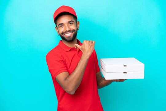 Pizza delivery Brazilian man with work uniform picking up pizza boxes isolated on blue background proud and self-satisfied