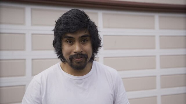 Young Man Looking Up And Smiling at Camera, Close-Up Against Garage Door