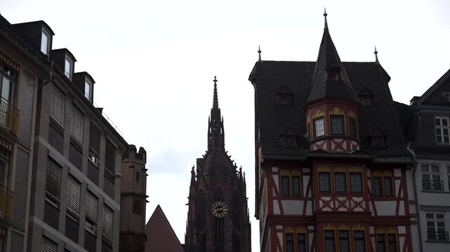 Haus zur Goldenen Waage and the Gothic tower of Frankfurt Cathedral rise between neighboring buildings under an overcast sky.