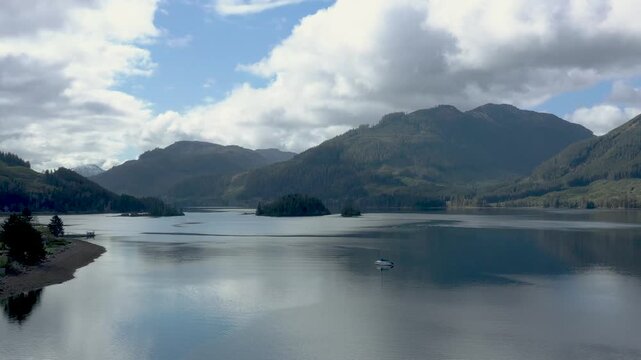 Still mountain lake with a lone boat drifting near forested hills and islands under a bright cloudy sky.