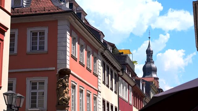 Row of colorful Heidelberg townhouses with a church tower rising behind them under a bright summer sky.