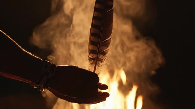 Hand holding feather over campfire at night, smoke and flames, tribal aesthetic