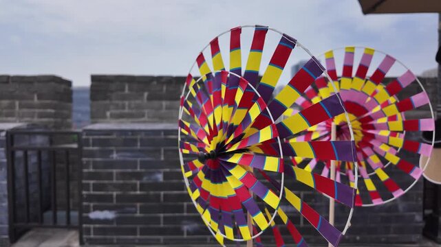 Vibrant multicolored pinwheel toys displayed against a gray ancient brick wall in an outdoor setting.