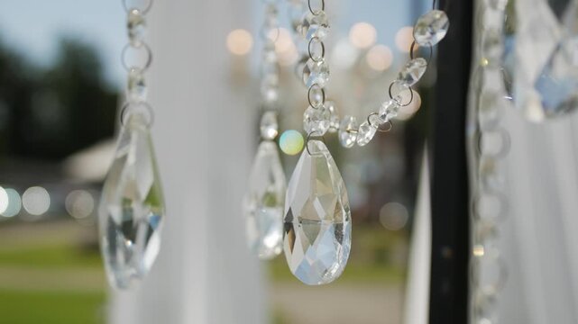 Chandelier adorned with crystal elements hangs amidst flowing fabric at a beautifully decorated outdoor wedding setting