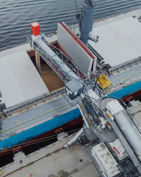 Riga, Latvia - 20 September 2021: Aerial view of a large cargo ship being loaded with grain at the port, featuring industrial loading equipment, conveyors, and the ship's open hold.