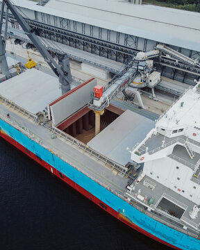 Riga, Latvia - 20 September 2021: Aerial view of a large cargo ship being loaded with grain at the port, featuring industrial loading equipment and storage facilities.