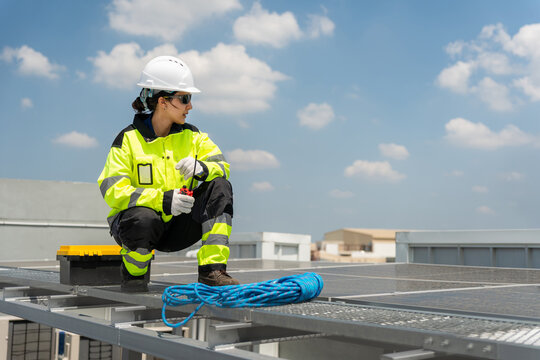 Female solar technician inspecting solar rooftop panels with radio, Worker working on solar energy installation, Renewable energy engineer performing maintenance on industrial solar rooftop array