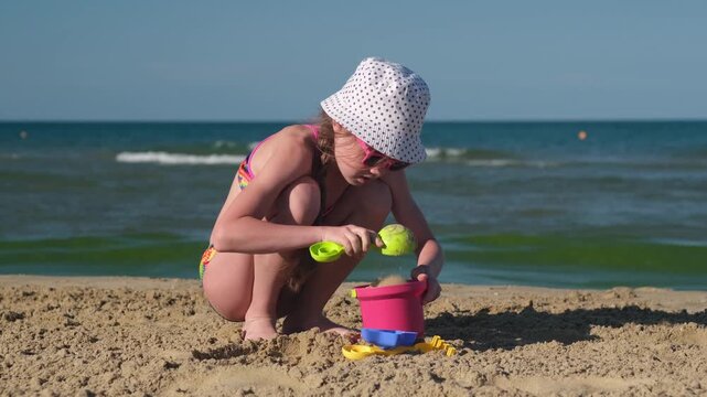 Young girl play with sand toys on beach. Childhood and summer vacation on ocean or sea coast concept. Kid having fun outdoors on family holidays. build sand castle