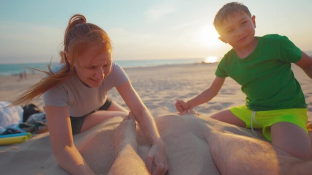 Mother and son build a sand sculpture on the beach at sunset