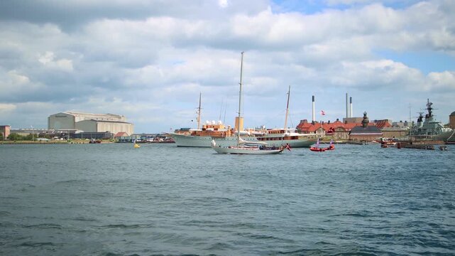 Royal yacht Dannebrog sailing in Copenhagen harbor with support vessels on summer day.