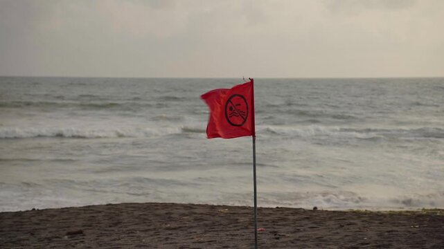 Red no swimming flag blowing in wind on a stormy beach