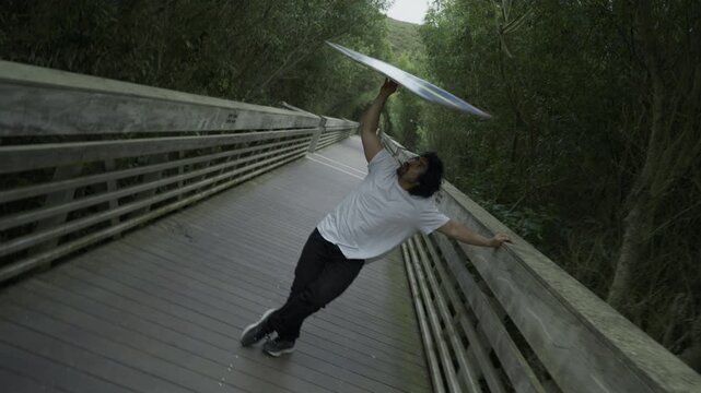Man Spinning And Tossing Painted Board Overhead on Wooden Footbridge - Steady Cam Tilt Shot