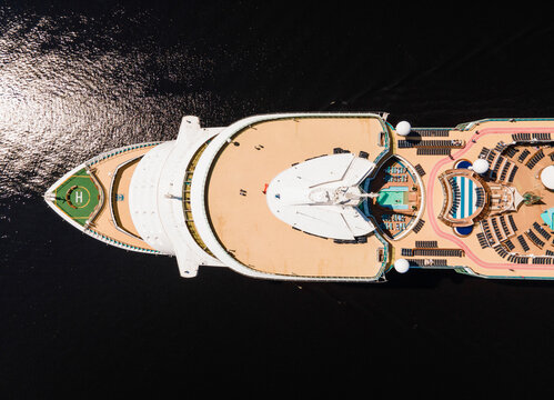 Riga, Latvia - 09 June 2022: Aerial view of a large cruise ship deck featuring a helipad, swimming pools, lounge areas, and sun loungers on the dark water.