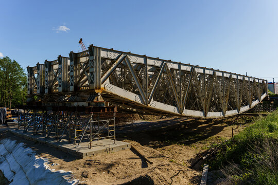 Massive steel bridge structure preassembled on the ground at a construction site, industrial metal framework supported by temporary scaffolding on dirt terrain, civil engineering, heavy infrastructure
