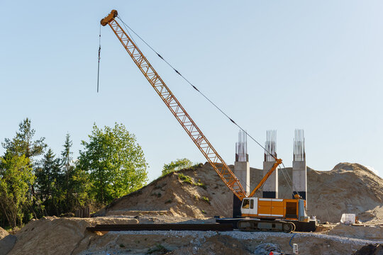 Large yellow crawler crane on an active construction site with bridge supports against a blue sky, infrastructure development, heavy lifting equipment, civil engineering, highway bridge construction