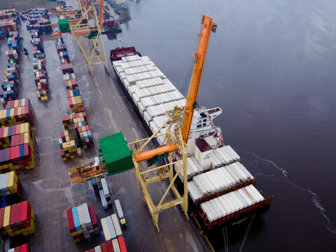Riga, Latvia - 23 March 2023: Aerial view of a container ship being loaded with cargo at the port terminal, featuring colorful shipping containers and large cranes.