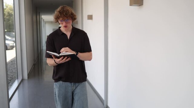 Vertical screen modern schoolboy studies while walking through school hallway reading notes before class showing how todays students work hard to achieve success