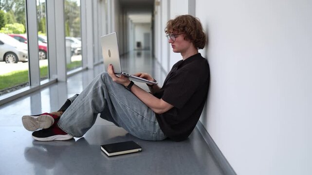 Vertical screen young man sitting on floor with laptop absorbed in gaming showing computer game addiction excessive screen time and digital dependence