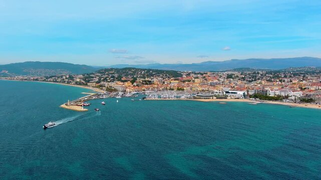 Aerial view of the bay of Cannes, France, with a boat entering the old port past the lighthouse jetty, moored yachts, the Palais des Festivals, La Croisette beach and hills of the French Riviera.