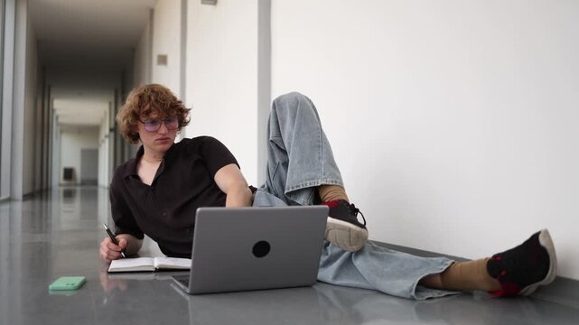 Vertical screen Young student gains knowledge while studying with laptop and notebook on office floor showing curiosity continuous learning education and focus