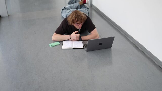 Vertical screen Young man studies on floor with laptop and notebook reflecting intensive education continuous learning academic workload and knowledge growth