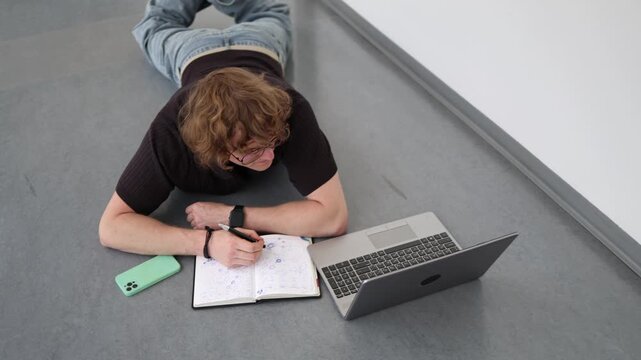 Vertical screen Student prepares for exam session lying on floor with notebook and laptop showing intensive revision determination and long academic study hours