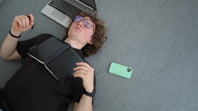 Creative professional lies on floor thinking through new ideas with notebook and laptop searching for inspiration solving complex problems and planning next steps
