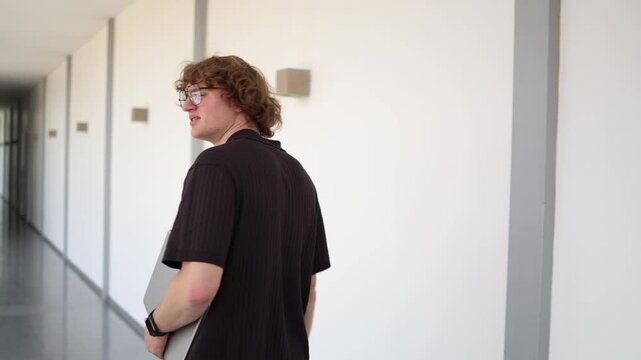 Young office worker leaves workplace carrying laptop after being fired showing disappointment uncertainty career setback and search for new opportunities
