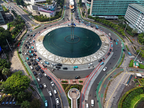 Menteng, Indonesia - 02 April 2026: Aerial view of Bundaran HI, a circular fountain and traffic roundabout surrounded by dense urban traffic, modern skyscrapers, and lush green trees.